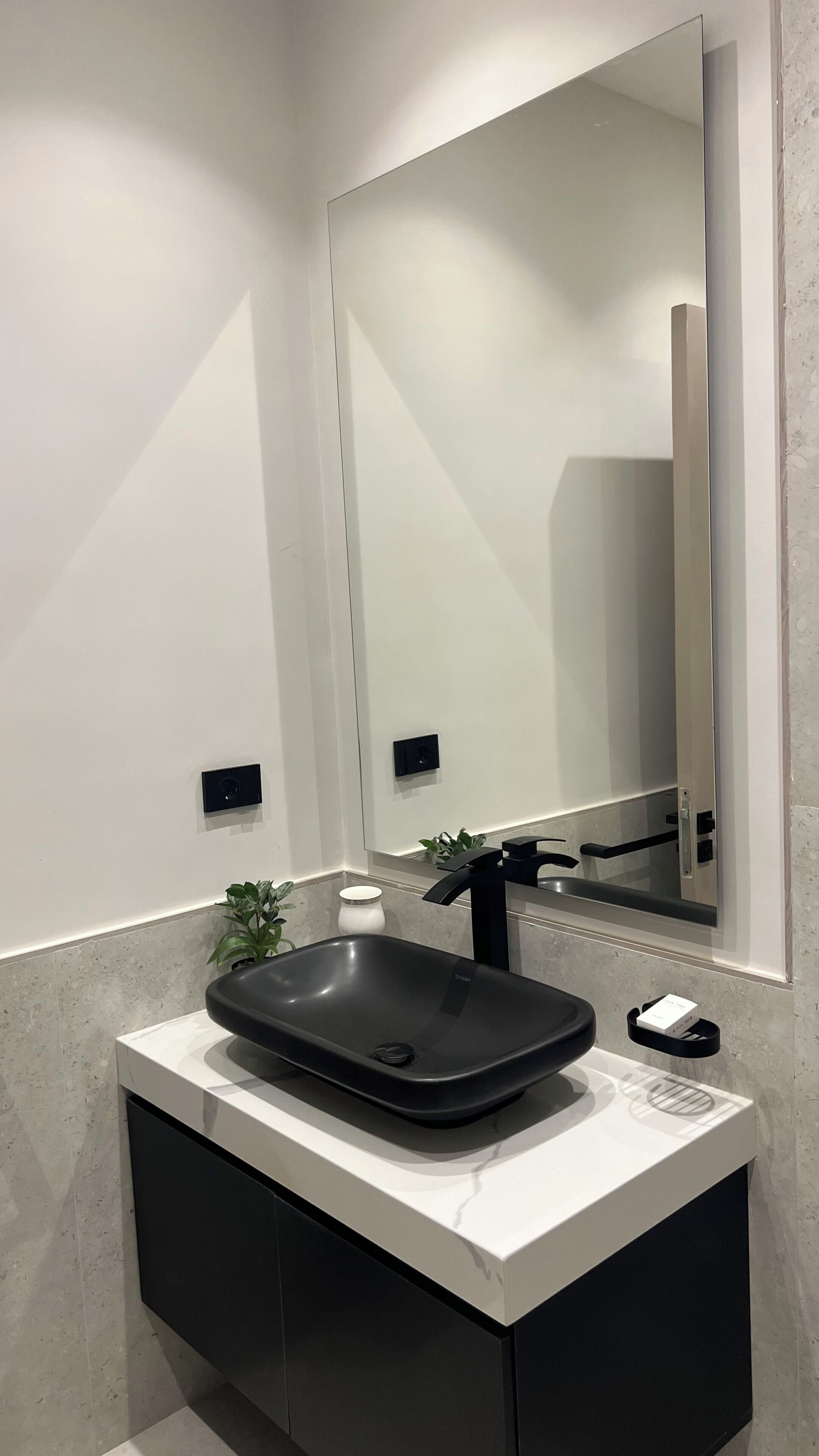 Ein modernes Badezimmer mit einem schwarzen Waschbecken, einem großen Spiegel und einer kleinen Pflanze.