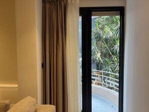 Una habitación con puerta de vidrio corrediza que da a un balcón con barandilla blanca y plantas verdes.