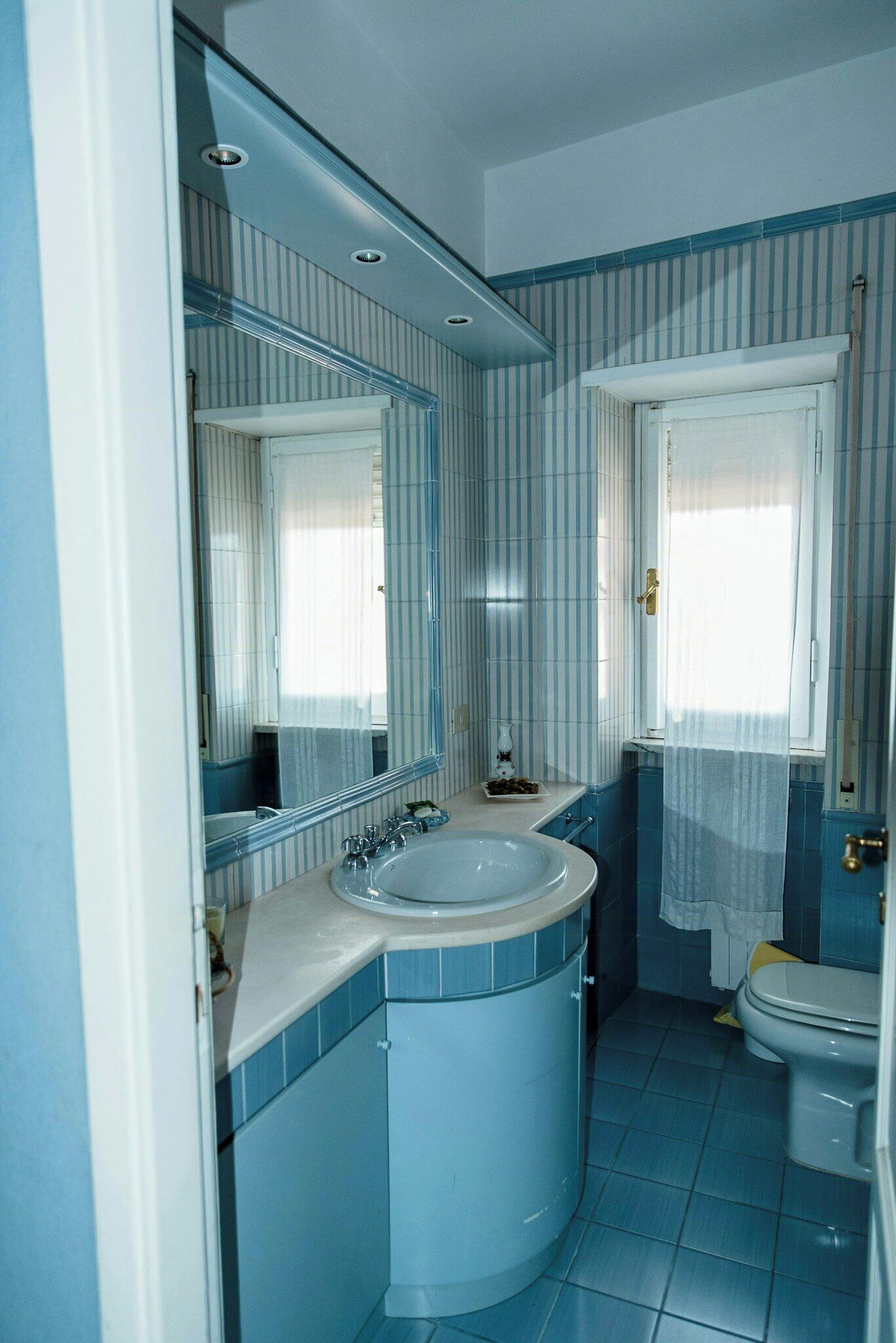 A bathroom with a sink, mirror, toilet, and window.