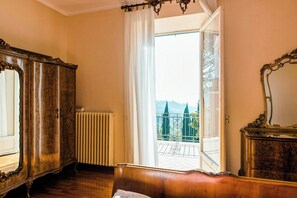 Una stanza con un letto di legno, un termosifone, una finestra vista balcone e uno specchio grande.