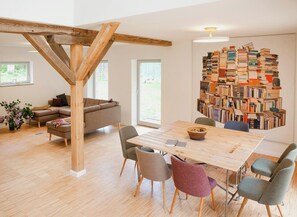 Ein zeitgemäßer Wohnraum mit sichtbarer Holzbalkenstruktur, einer Couch, einem Esstisch mit Stühlen und einer Bücherregalwand.