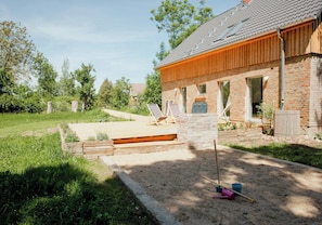 Ein Backsteinhaus mit einer Holzdielen-Terrasse, einem Steinpfeiler und einem Sandkasten mit Schaufel und Eimer.