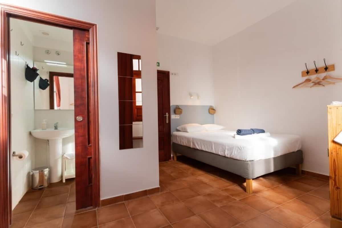 Une chambre à coucher comprenant un lit, une armoire en bois, un miroir et une salle de bain avec un lavabo et des toilettes.