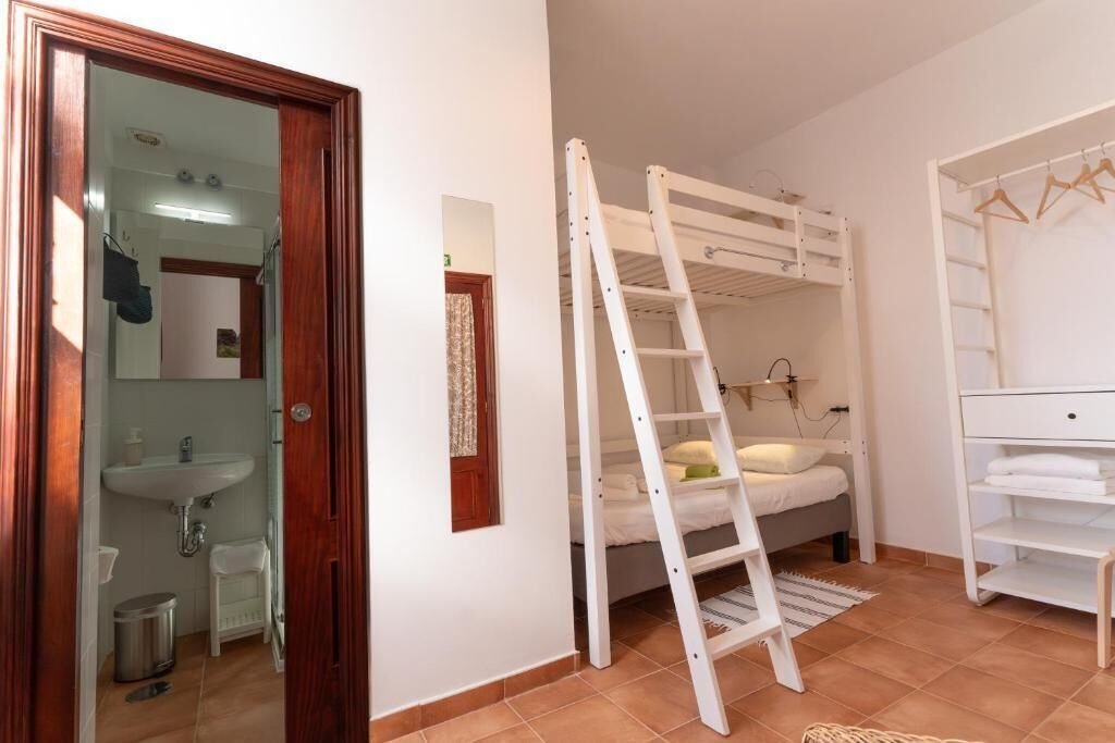 Un dormitorio con una cama litera, una escalera, un tocador blanco y un baño con lavabo y espejo.
