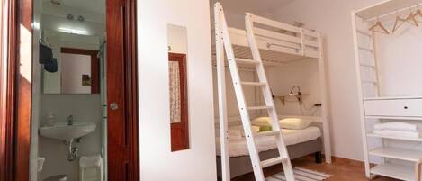 Un dormitorio con una cama litera, una escalera, un tocador blanco y un baño con lavabo y espejo.