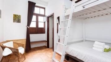 Une pièce avec un lit superposé, une chaise, une échelle, une fenêtre avec des rideaux et une porte.