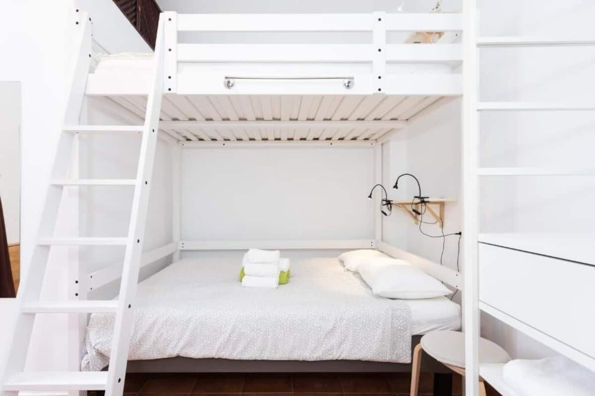 Une chambre avec un lit superposé, une échelle, une petite table et une étagère fixée au mur.
