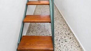 Un escalier étroit avec des marches en bois et des rampes de garde-corps en métal, menant à une porte sur laquelle est apposée une enseigne.