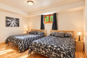 A room with two beds, a window with curtains, a wall-mounted lamp, and a framed picture. - Chalet Brise du Nord (Matawinie Regional County Municipality)