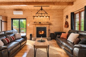 L’intérieur chaleureux d’un chalet avec deux canapés en cuir, une cheminée et un plafond en bois.