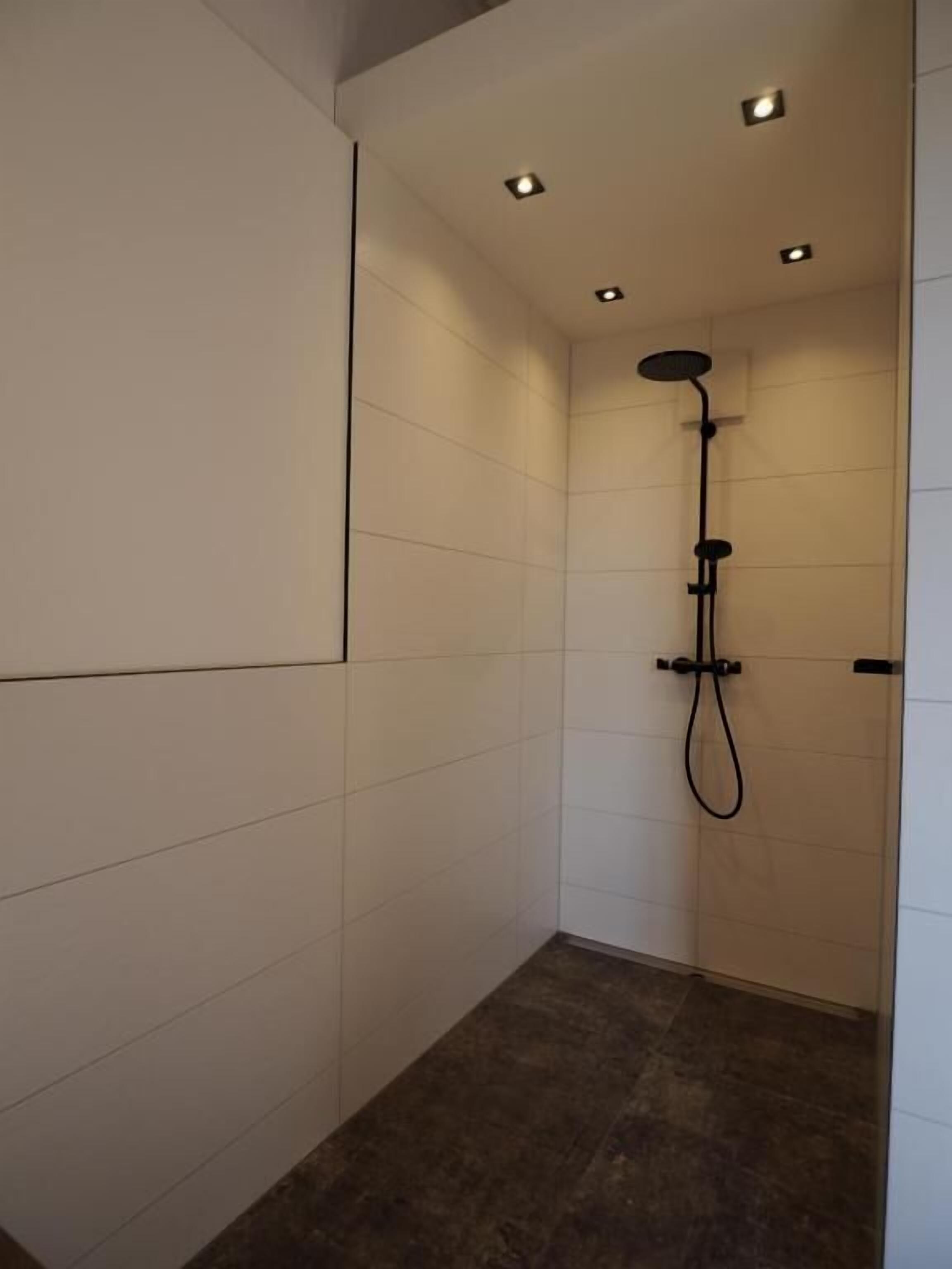 Ein modernes Badezimmer mit weißen Fliesenwänden, dunklem Boden und Einbaustrahlern.