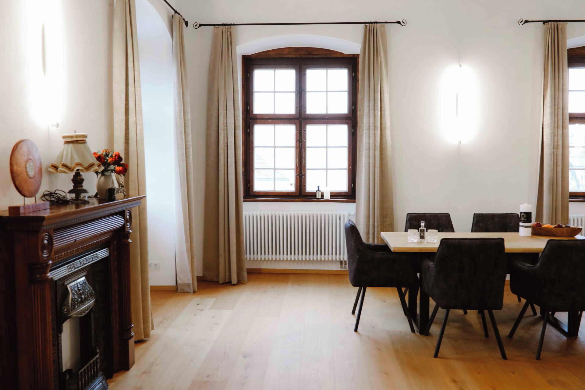 Zona pranzo con tavolo e sedie, termosifone e finestra con tende.