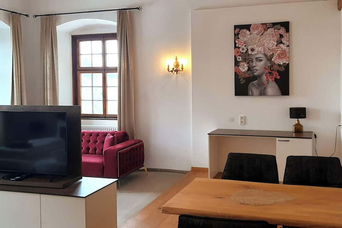 A modern living room with a TV, red sofa, dining table, and a painting on the wall.