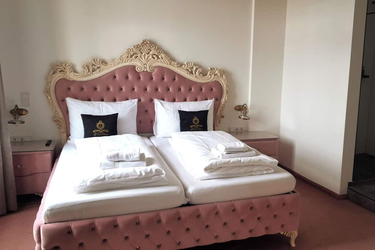 A double bed with a tufted headboard, two white pillows with a black accent, and a neatly made bed with folded white towels.