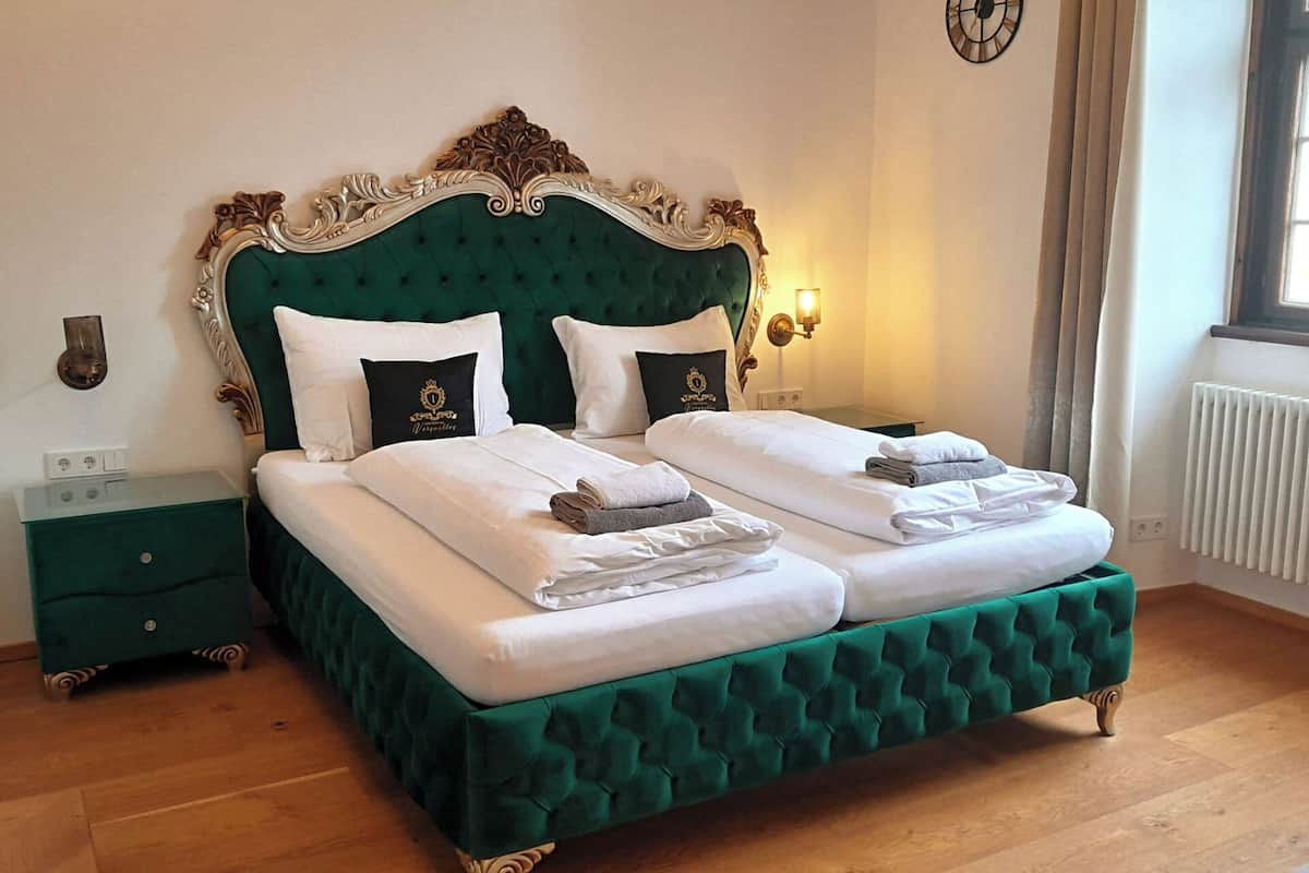 A double bed with a green upholstered headboard, white linens, and two pillows.