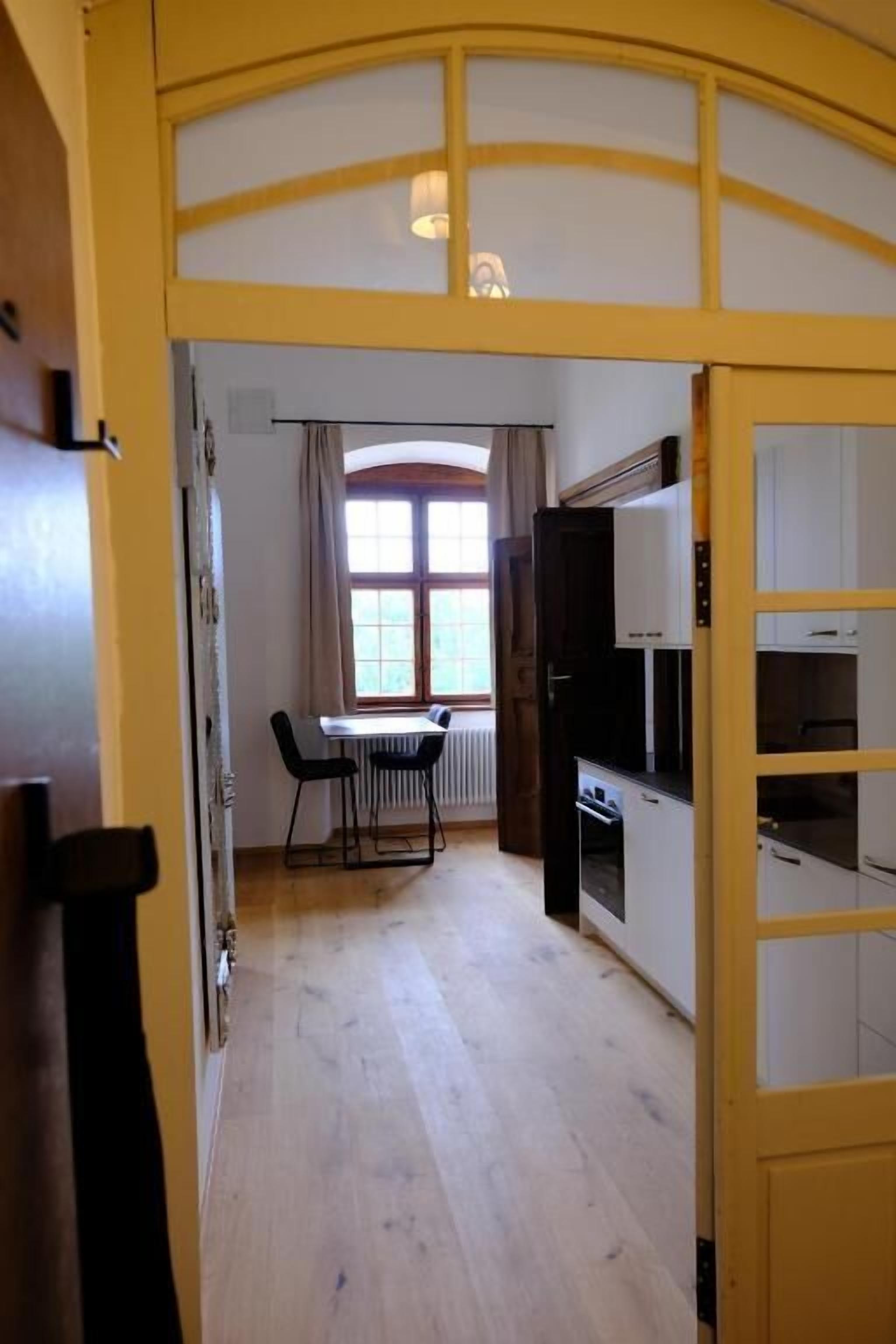 A room with a dining table and chairs, a window with curtains, and built-in kitchen cabinets.
