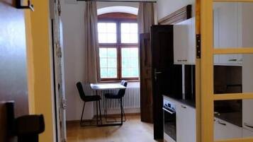 A room with a dining table and chairs, a window with curtains, and built-in kitchen cabinets.