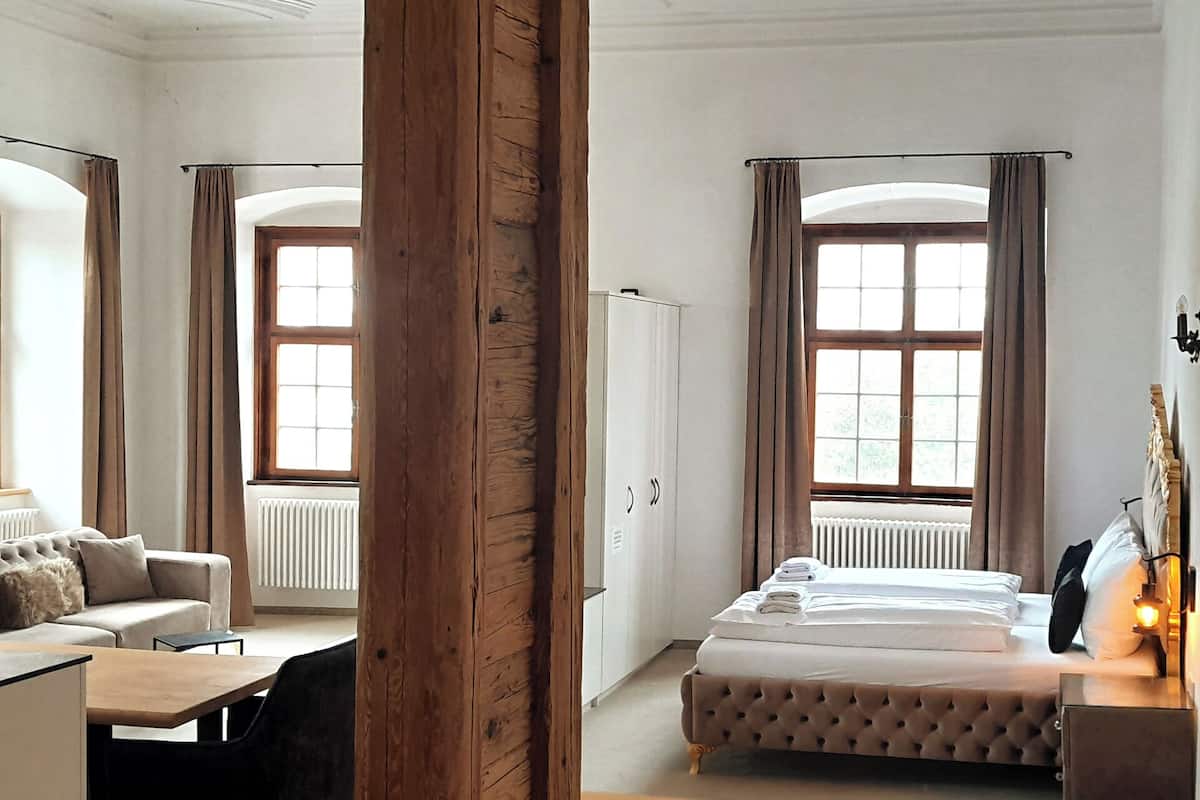 A hotel room with a bed, a sofa, a desk, and a window with curtains.