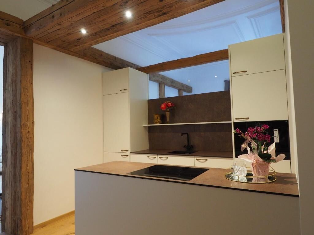 Eine moderne Küche mit einer zentralen Kochinsel, Holzbalken an der Decke und Blick zum Himmel.