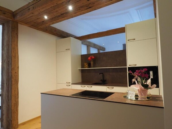 Une cuisine moderne avec un îlot central, des poutres en bois au plafond et une vue sur le ciel.