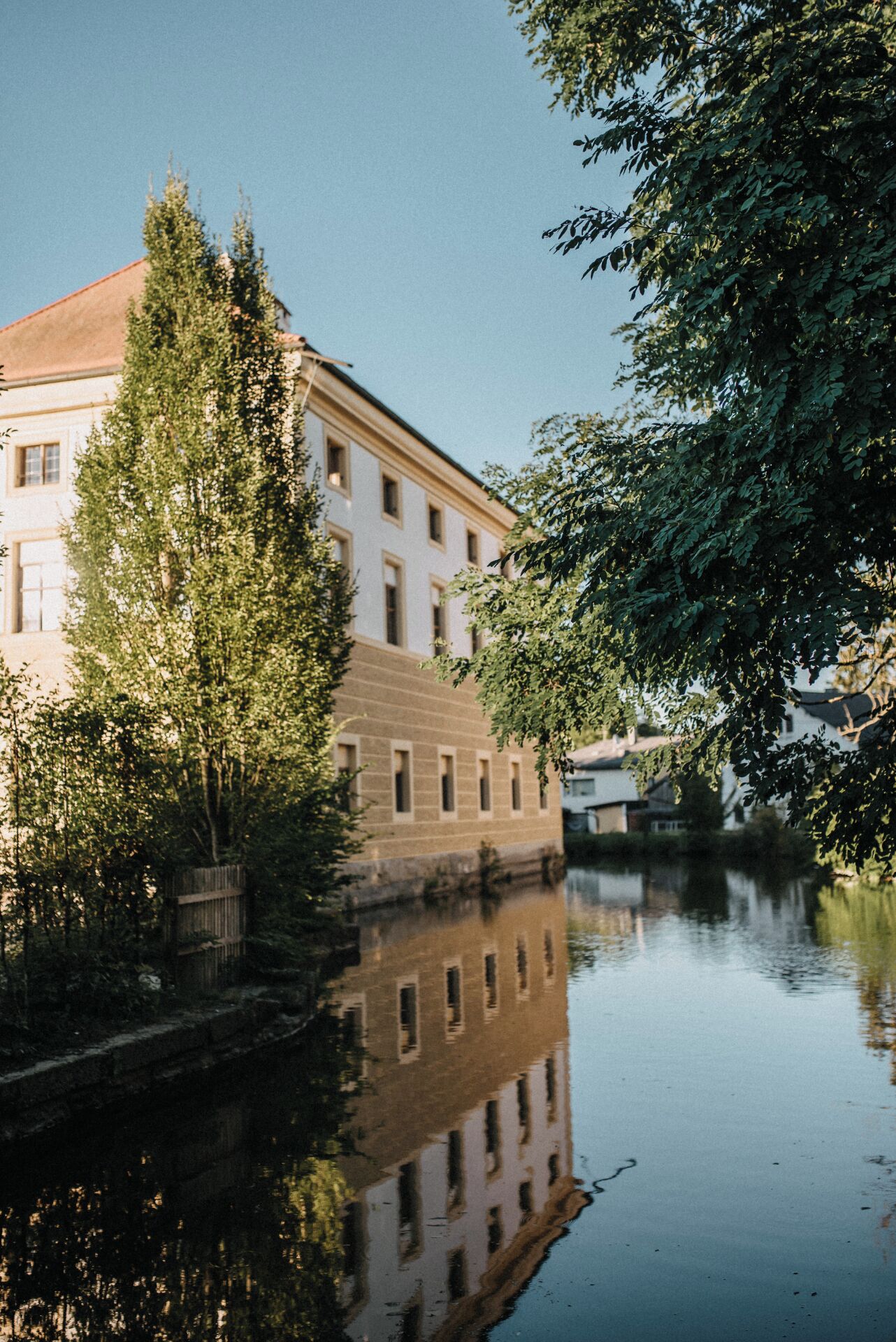 A building with a reflection in calm water, surrounded by trees.