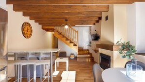Eine moderne Küche mit einer Holztreppe, einem Essbereich mit Tisch und Stühlen sowie einem Wohnzimmer mit Kamin.