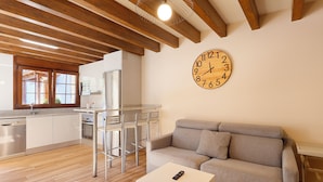 Eine moderne Küche mit Holzbalken, einem Essbereich mit Stühlen, einem Sofa und einer Wanduhr.