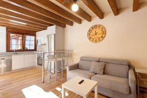 A modern kitchen with wooden beams, a dining area with chairs, a sofa, and a wall clock.