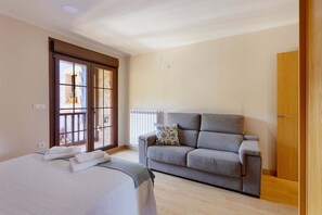 Ein Schlafzimmer mit einem Bett, einem grauen Sofa, einem Holzschrank und einem Fenster mit Blick.