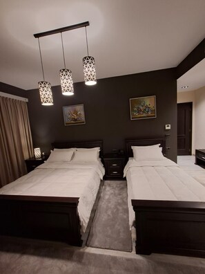 A double bed room with a dark wall, two bedside tables, a nightstand, a painting, and three pendant lights.
