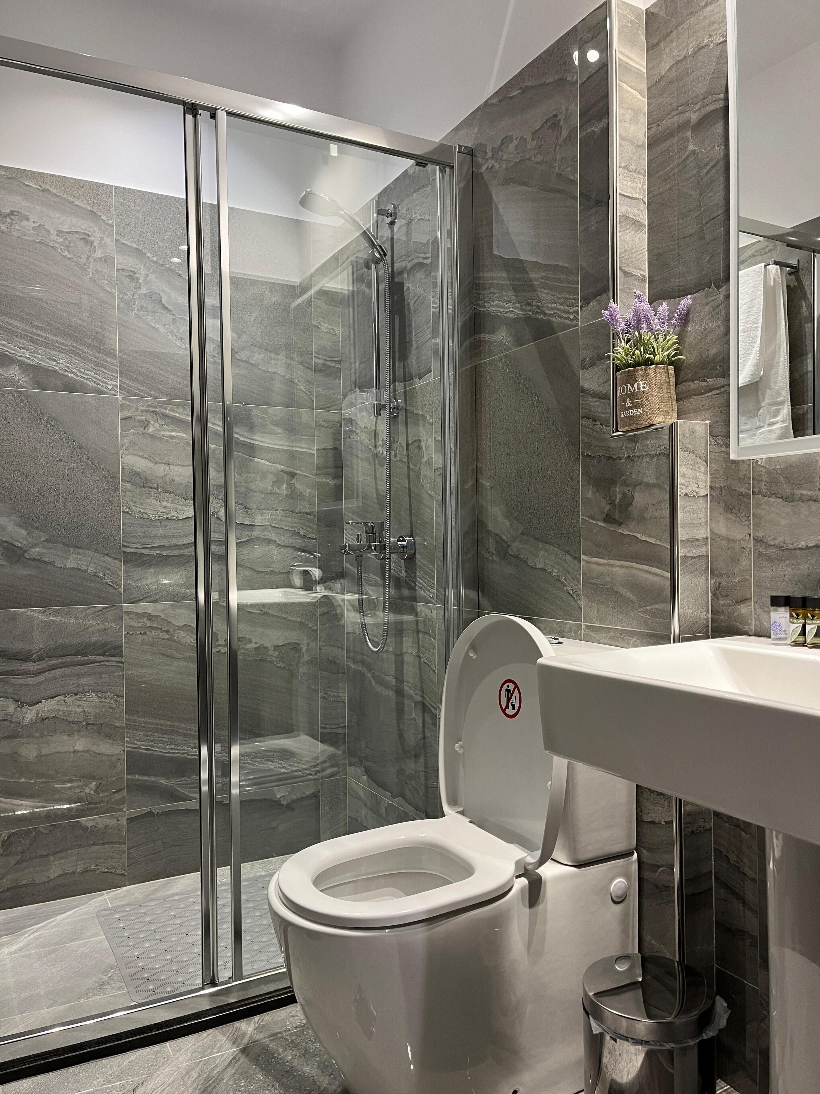 A modern bathroom with a glass-enclosed shower, a white toilet, and a marble-tiled wall.