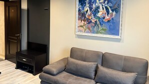 Ett modernt vardagsrum med en grå soffa, ett mörkt träskåp och en inramad abstrakt målning på väggen.