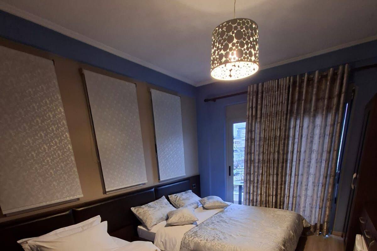 Habitación de hotel con dos camas, un ventanal con cortinas, una lámpara en el techo y suelo de madera.