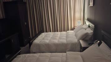 Una habitación de hotel con dos camas, un armario, un televisor y una ventana con cortinas.