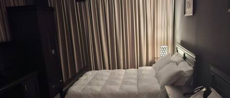 Ett hotellrum med två sängar, en garderob, en tv och ett fönster med gardiner.