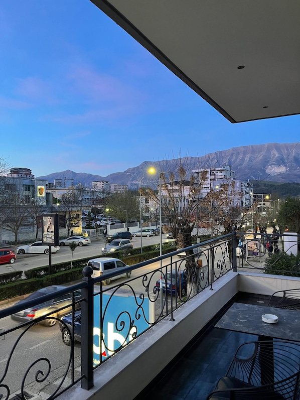 A balcony with a view of a city street, buildings, and mountains.