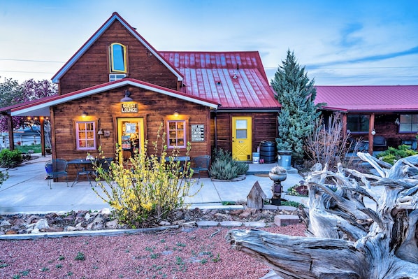 A rustic wooden building with a red roof, a yellow door, and a sign indicating guest rooms and a guest lounge.