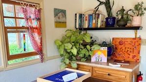 A wooden table with a blue tray, a bookshelf with books and plants, a window with curtains, and a fire extinguisher. - Boutique Retreat, Canyon Room (Escalante)