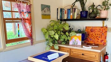 Una mesa de madera con una bandeja azul, una estantería con libros y plantas, una ventana con cortinas y un extintor.
