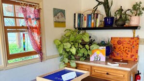 Ein Holztisch mit einer blauen Tablett, ein Bücherregal mit Büchern und Pflanzen, ein Fenster mit Vorhängen und ein Feuerlöscher.