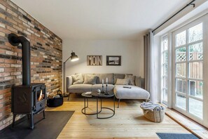 A living room with a brick wall, a black wood-burning stove, a sofa, a coffee table, and a large window. - Historic house in Gammendorf on Fehmarn (Fehmarn)