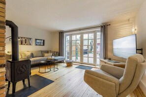 A cozy living room with a fireplace, a sofa, a TV, and a large window. - Historic house in Gammendorf on Fehmarn (Fehmarn)