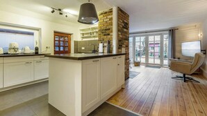 Una cucina moderna con isola centrale, mobili bianchi, una parete decorata con mattoni e un'area pranzo con una sedia.