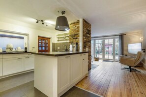 A modern kitchen with a central island, white cabinetry, a brick accent wall, and a dining area with a chair. - Historic house in Gammendorf on Fehmarn (Fehmarn)