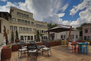 An outdoor patio with wooden flooring, metal chairs, and tables, surrounded by buildings. - Minia Cave Hotel Ortahisar (Ürgüp)
