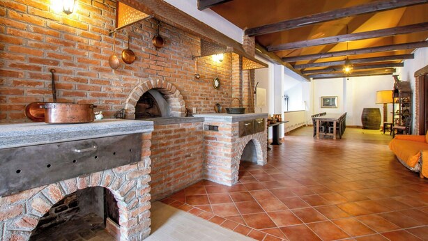 A rustic kitchen with a brick oven, wooden beams, and a tiled floor.