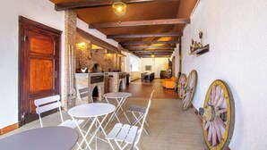 A rustic interior with exposed wooden beams, a brick fireplace, and a dining area with white chairs and tables.