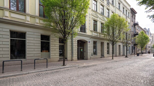Calle adoquinada flanqueada por edificios históricos, con amplios ventanales y una acera arbolada.