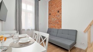 Un comedor con una mesa blanca para cuatro personas, un sofá gris y una pared de ladrillo.