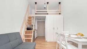 Un espacio habitable compacto con sofá, mesa de comedor, sillas, una escalera y una zona de cocina.